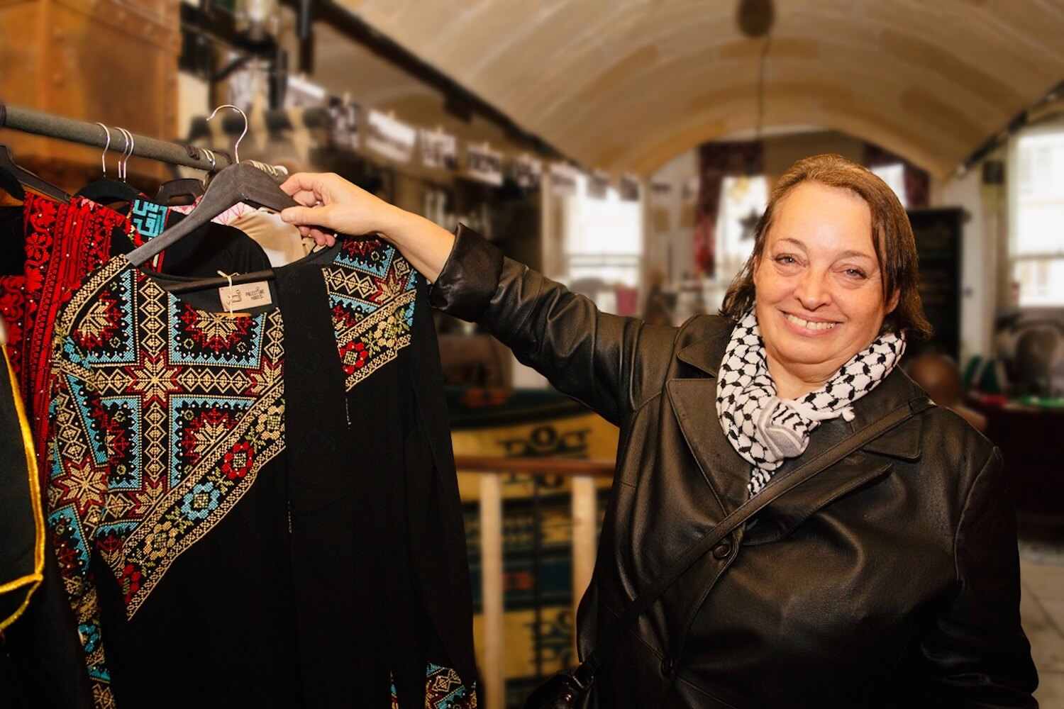 Tour guide holding a traditional Palestinian tatreez dress at a cultural shop in London.