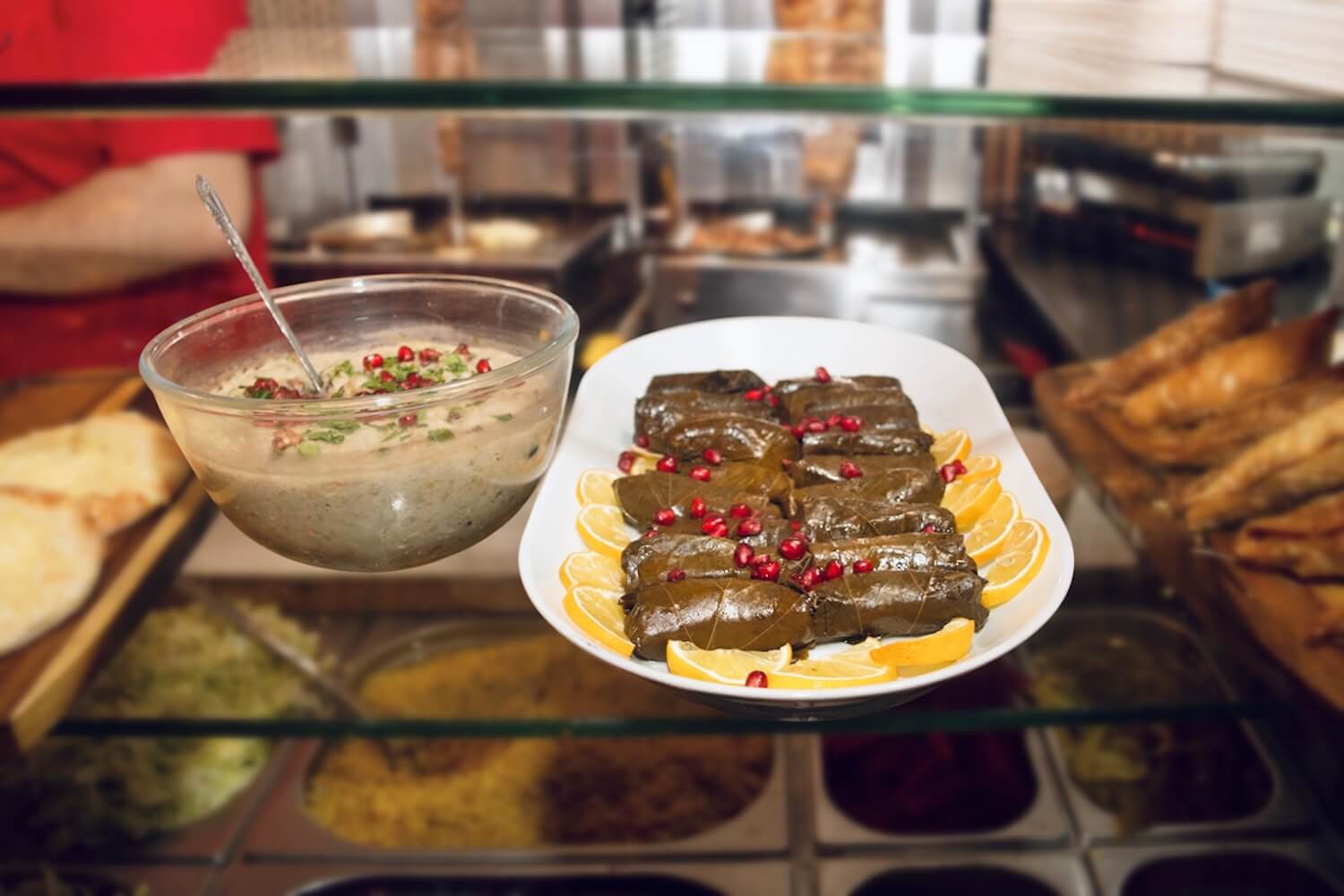 Palestinian mezze at Love Falafel: bowl of creamy dip and stuffed vine leaves topped with pomegranate seeds and lemon slices.