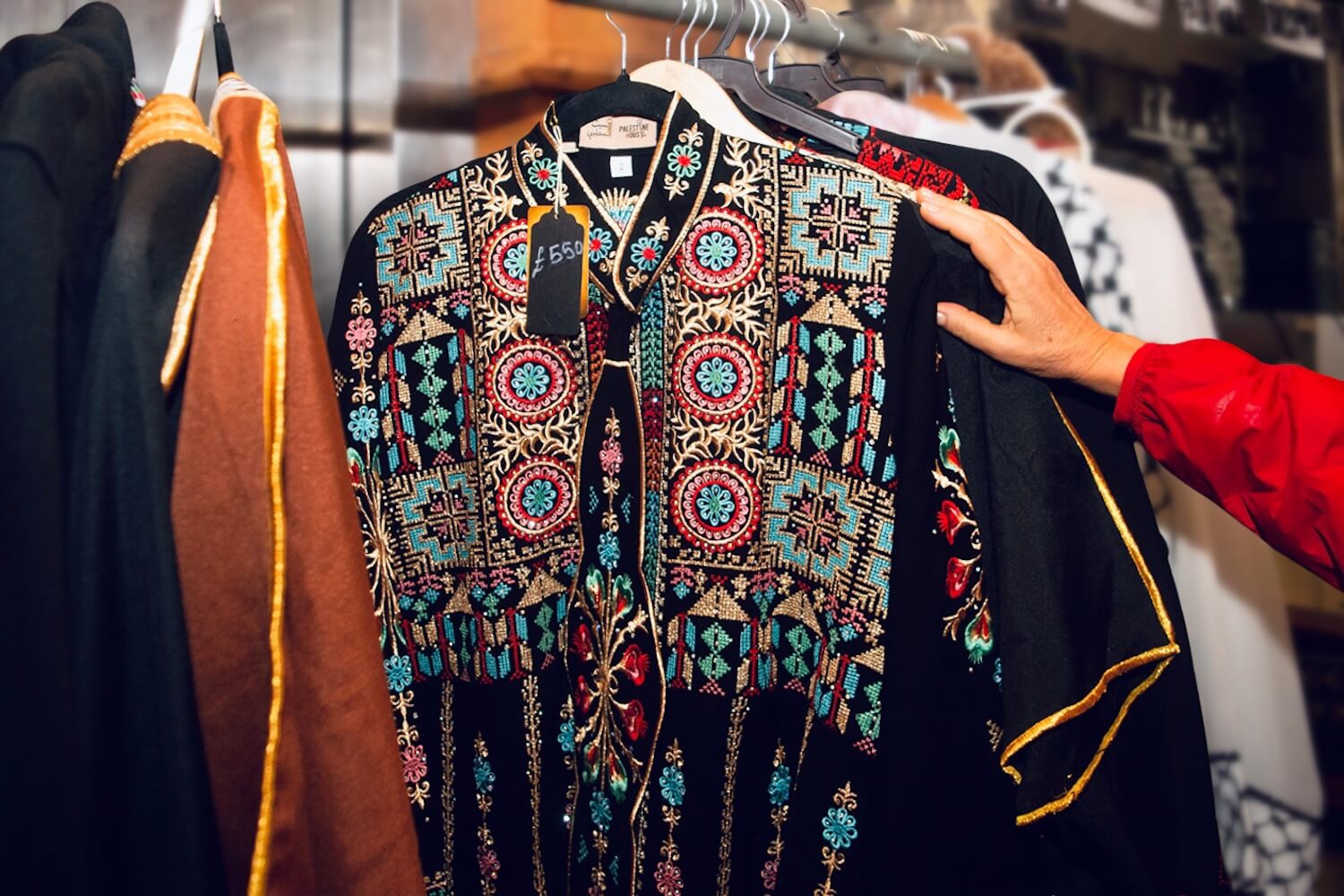 Traditional Palestinian tatreez thobe on a hanger, richly embroidered in red, blue and gold, displayed at Palestine House.