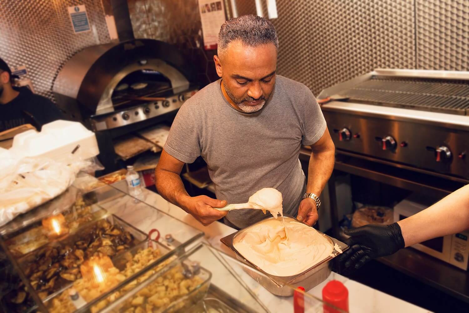 Chef scooping creamy hummus at Love Falafel, a stop on the Palestinian culture tour.