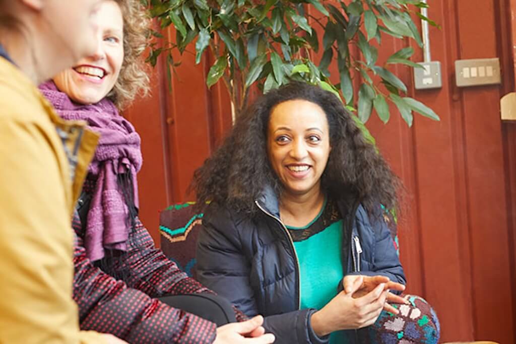 Your local tour guide, Sefanit, siting on a chair next to her guests on a tour, inside a coffee shop in London's Shepherd’s Bush neighbourhood.