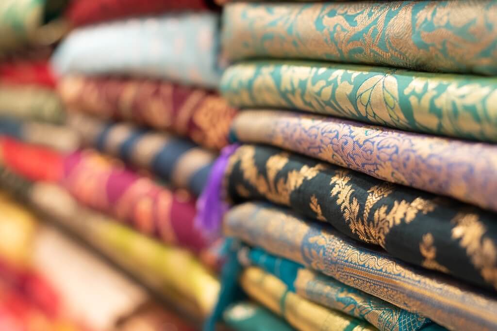 Ornate Indian textile piled on a shelf at at Indian textile store in London that we visit on our Indian Community of London Tour with Vaishali.