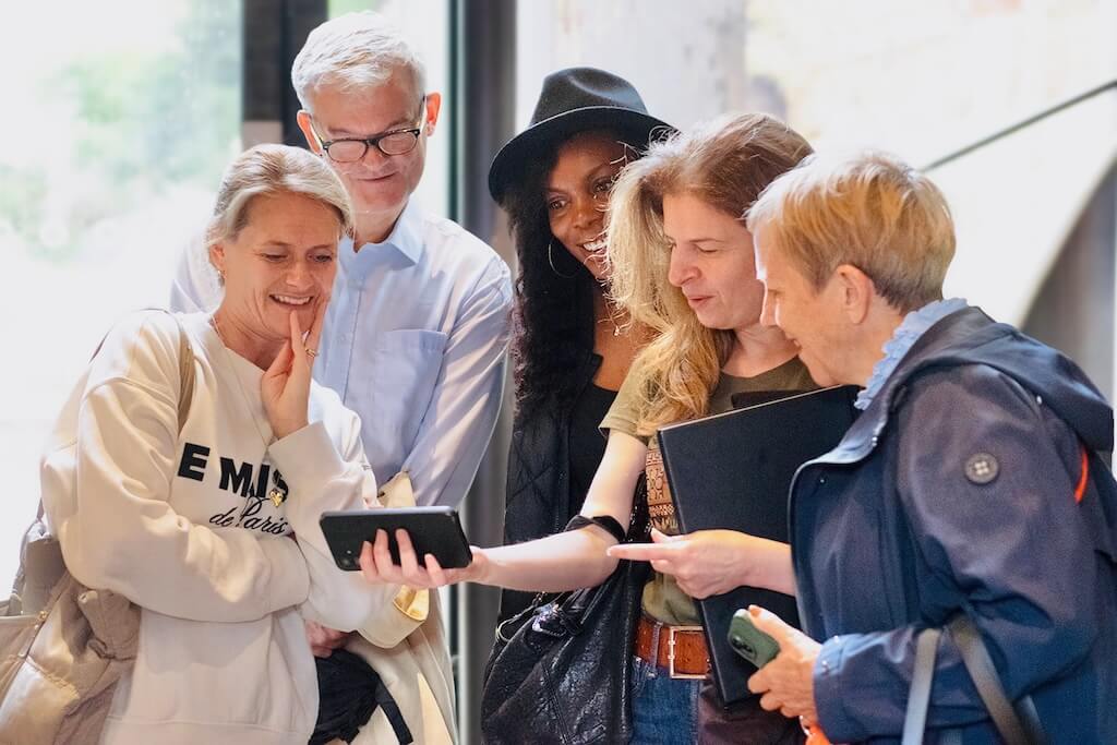 Group of tour participants gathered around guide Nadia, looking at a phone together and sharing a moment of discovery.