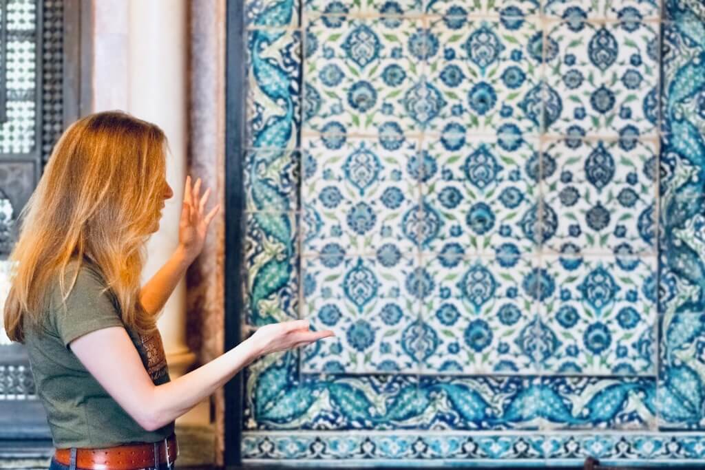 Nadia explaining the intricate blue and white Damascene tilework inside a heritage-inspired setting.