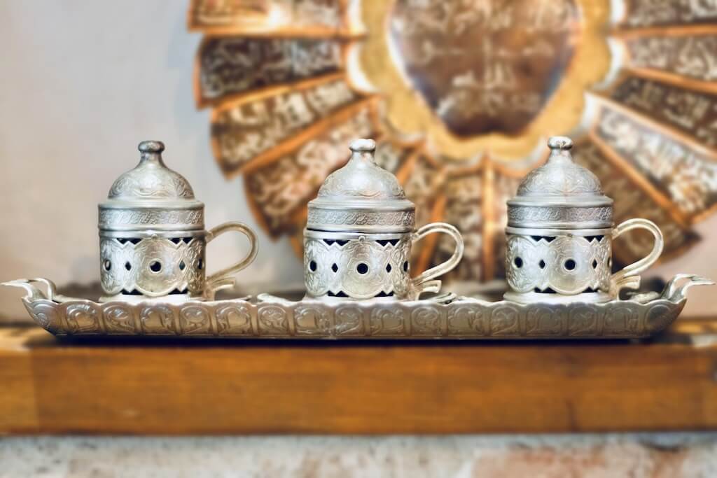 Decorative silver Arabic coffee cups with lids displayed on a tray, part of the cultural artifacts seen on the tour.