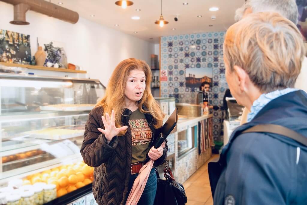 Guide Nadia speaking passionately to participants inside a Levantine café, surrounded by traditional décor.