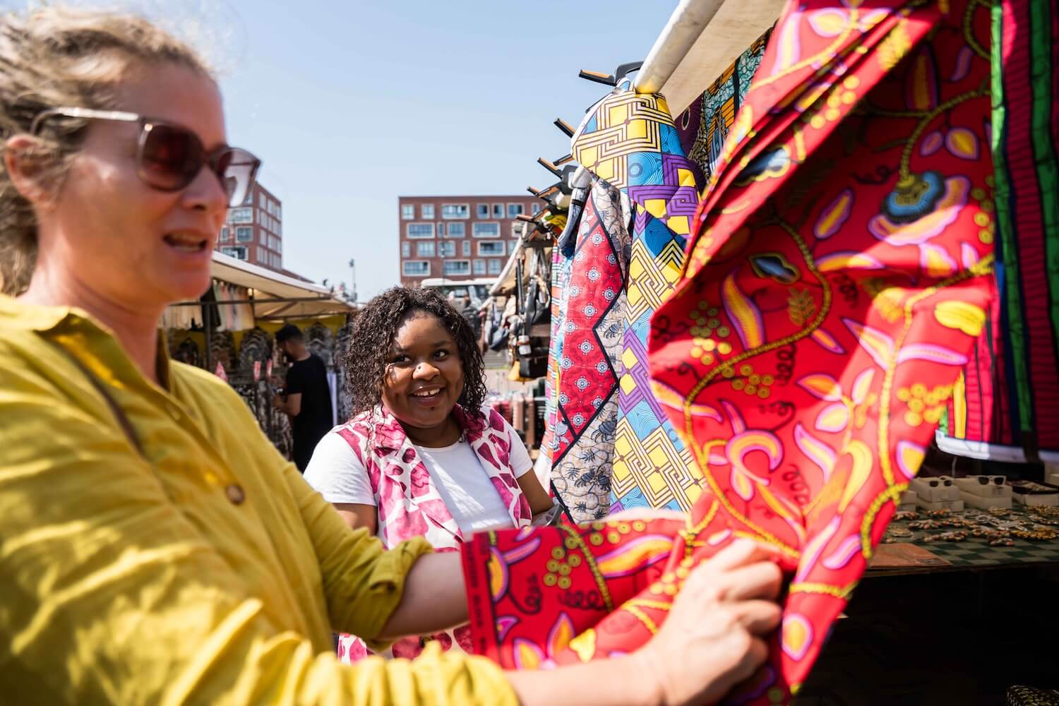 Tour guide and guest browsing colourful African-print fabrics at a market in Amsterdam Zuidoost.