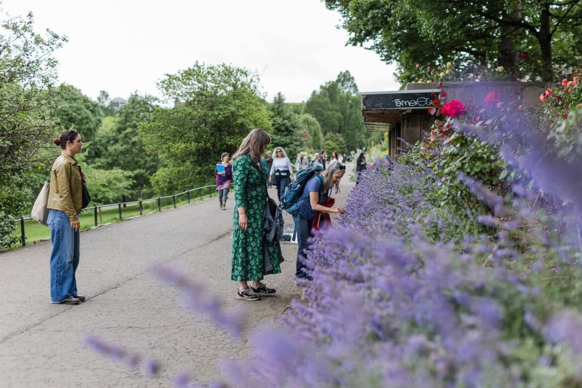Tour guests pausing to smell purple flowers during a women-led nature walking tour in Edinburgh.