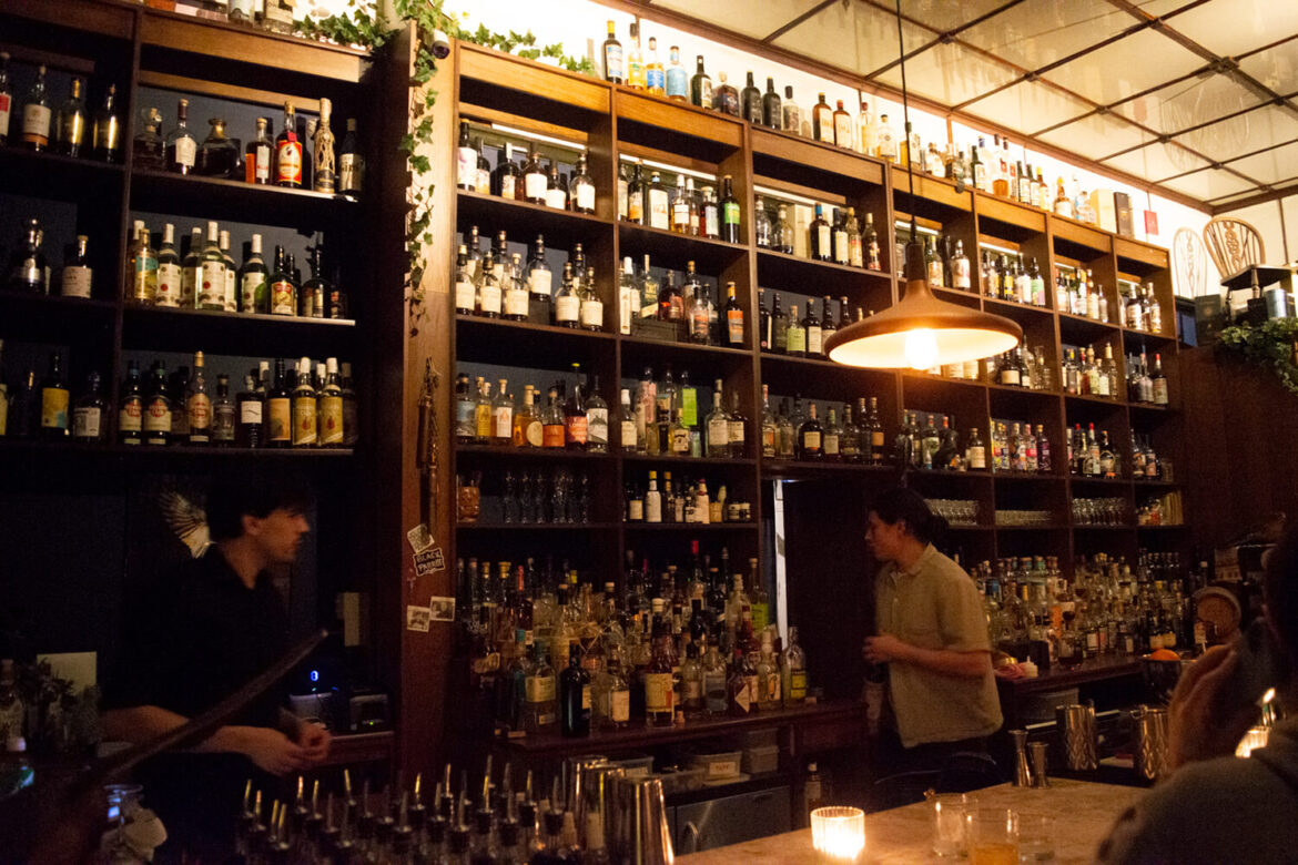 Atmospheric cocktail bar interior with shelves of spirits on a London food history tour exploring migration and flavour.