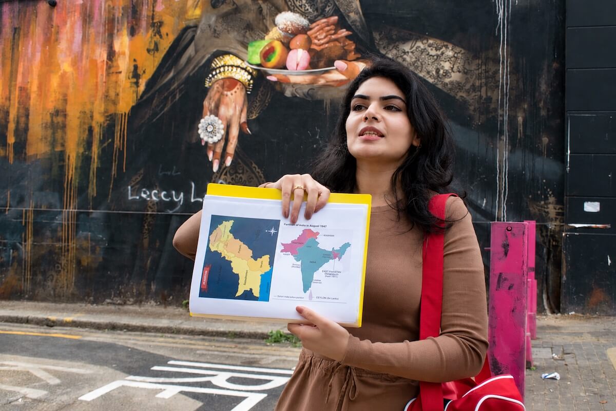 Tour guide Fatima holding a map of the 1947 Partition of India in front of a street mural in East London