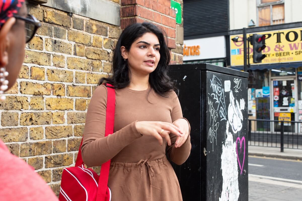Female tour guide Fatima in a brown dress talking to guests on an East London street at the start of the Pakistani diaspora tour