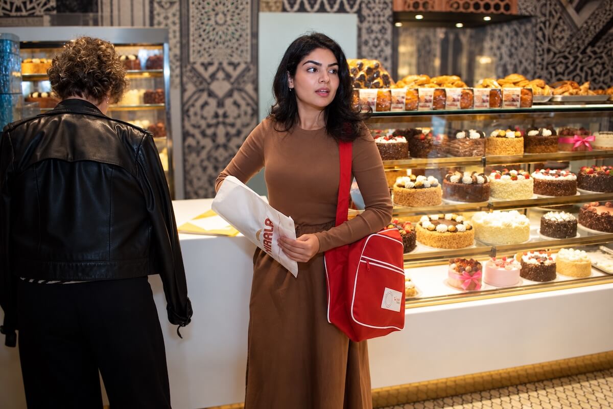 Tour guide Fatima beside a glass display of cakes and pastries at a Pakistani sweet shop in East London