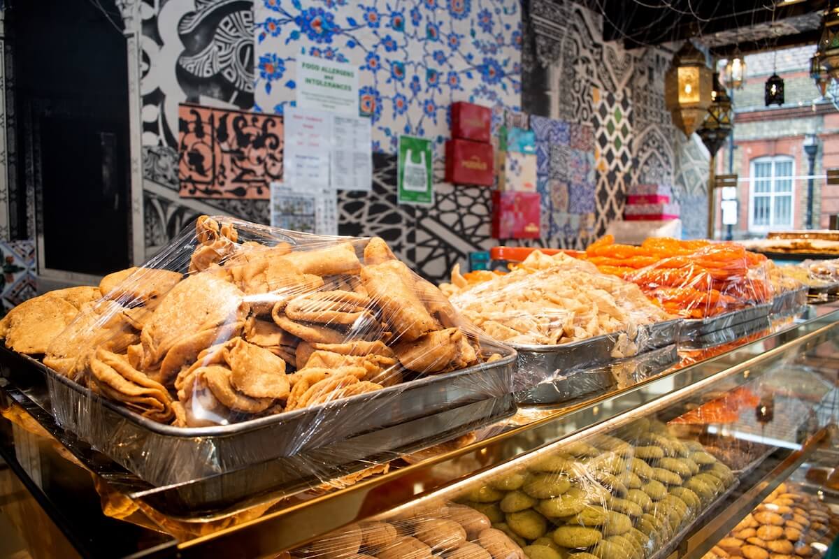 Trays of fried savoury pastries, jalebi and traditional sweets on the counter of a Pakistani sweet shop in East London