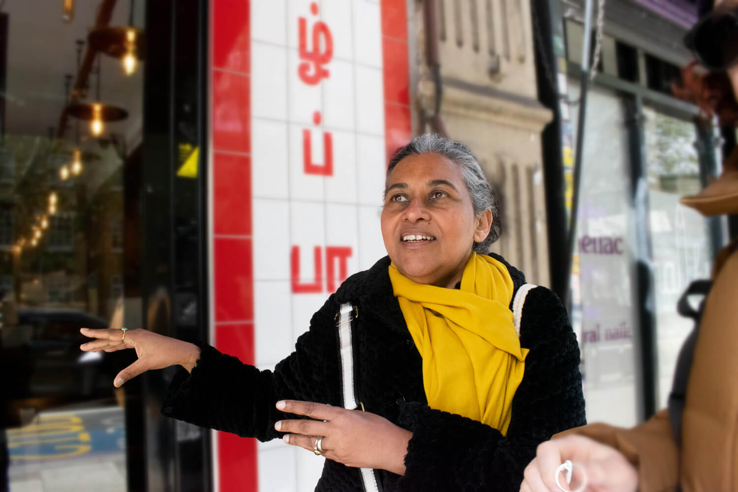 Guide Ranji speaking outside Jaffna House in Tooting, with Tamil writing behind her