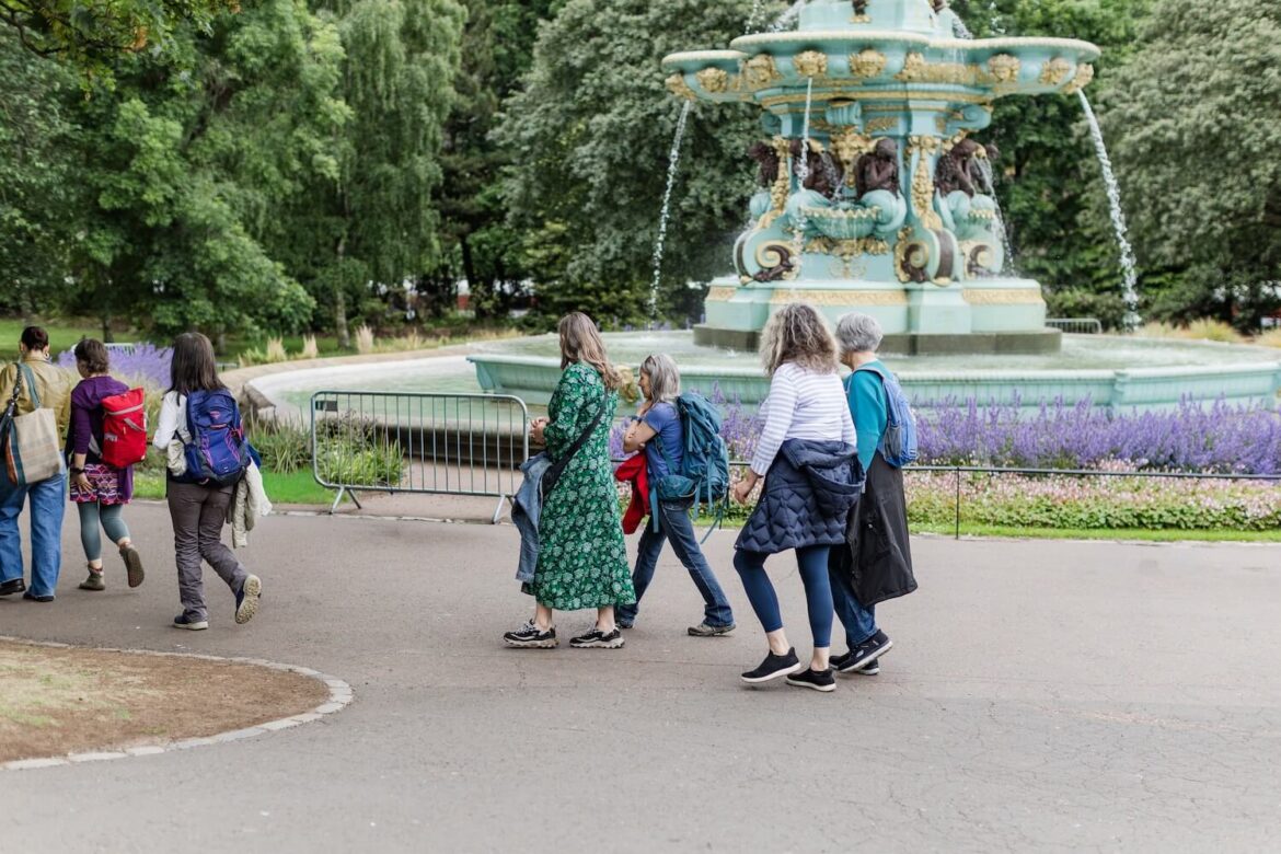 Women walking past the turquoise Ross Fountain and flower beds in West Princes Street Gardens, Edinburgh.