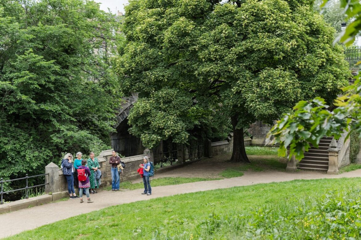 Martina speaking with a small group beneath mature trees beside the Water of Leith during an Edinburgh nature tour.