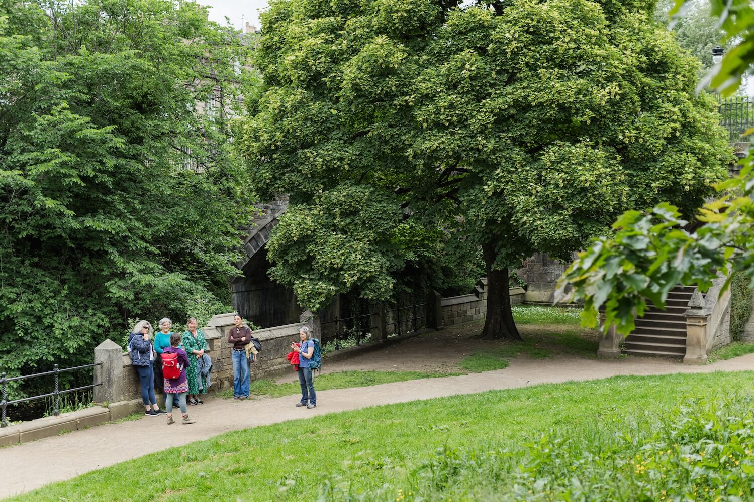 Martina speaking with a small group beneath mature trees beside the Water of Leith during an Edinburgh nature tour.