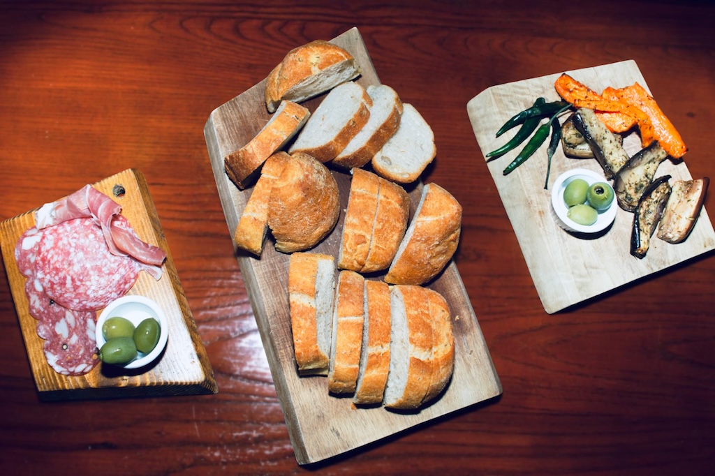 Traditional Iberian tapas served on wooden cutting boards with cured ham, salami, baked eggplant and peppers, olives and freshly-baked bread.