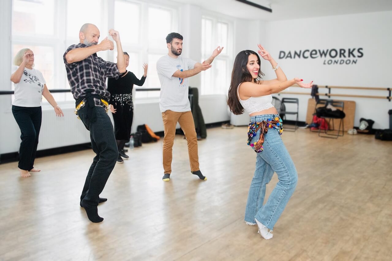 Amal leading a belly dancing class at Danceworks London, with participants of different ages following her movements in a bright studio.