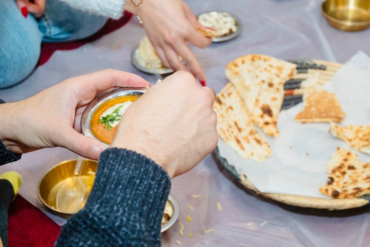 Close-up of a guest dipping bread into a traditional Saudi dish, while others share food in a communal dining experience.