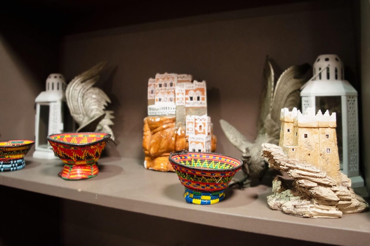 Shelf display of traditional Saudi handicrafts and souvenirs, including woven baskets, miniature buildings, and decorative lanterns.
